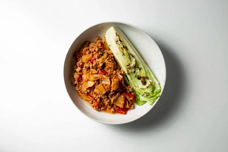 Cooked meat and vegetable dish served in a white ceramic bowl with grilled lettuce on a clean white background
