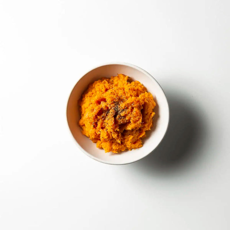 Orange-yellow mashed vegetable puree served in a small white ceramic bowl on a clean white background with a soft shadow