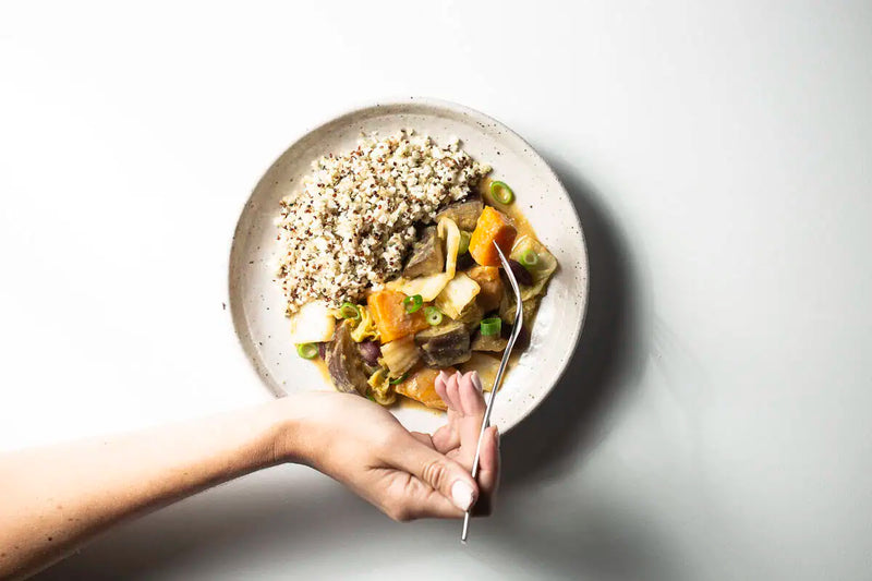 Quinoa served with a hearty vegetable stew on a speckled ceramic plate with a fork on a clean white background