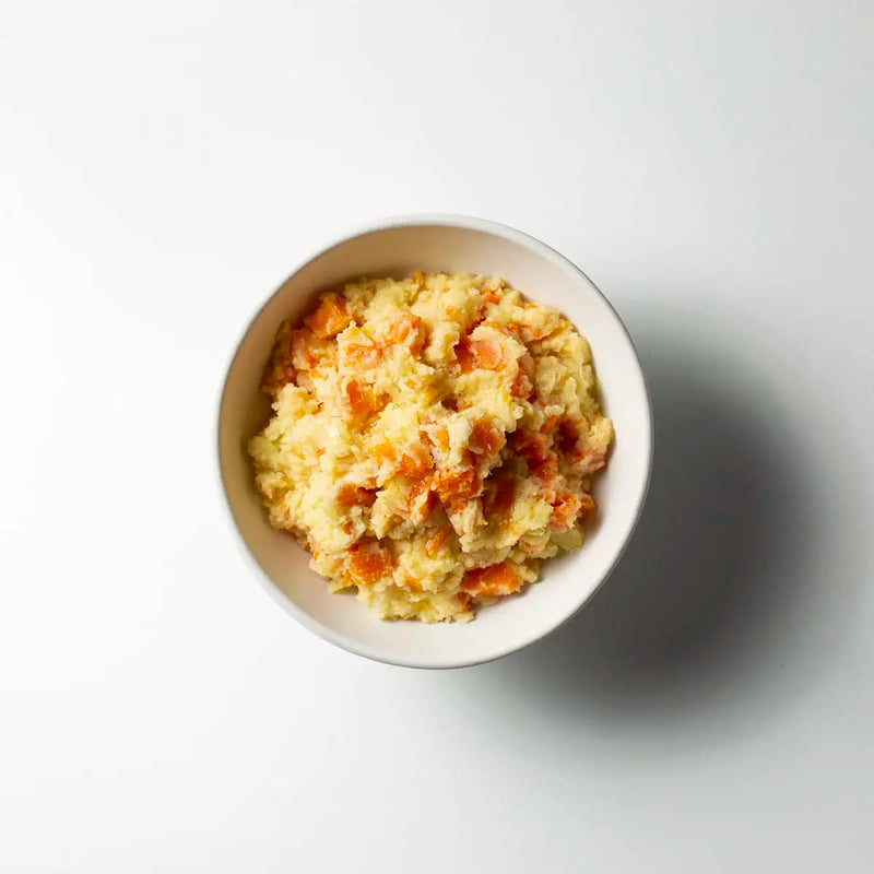 Creamy yellow mashed sweet potato and carrot dish served in a white ceramic bowl on a light gray background.
